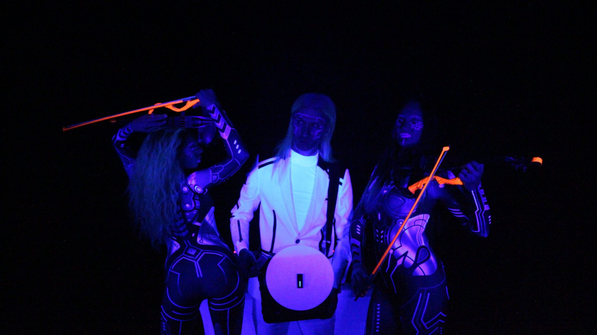 3 musicians lit UV Lights creating neon glow on their catsuits and corporate dress whites. dj holding portable turntable Violinists holding glow in the dark violins #vynilyn #lrbaggs #cordialcablesusa #codabow #thomastikinfeld #dollskillclothing #yamahaelectricviolin #justfabstyle #yamahamusic #electricviolin #electricviolinists #electricviolinist #aliens👽 #notfromthisworld #dancingviolinist #djculture #djviolinist #djviolin #femaleartist #femalemusicians #longhairedman #followusonyoutube #vinylart #bookmorewomen #eventplanner #eventplanning #eventprofs #meetingprofs #corporateeventplanner #meetingplanner #corporateevent #zoomhappyhour #virtualevents 