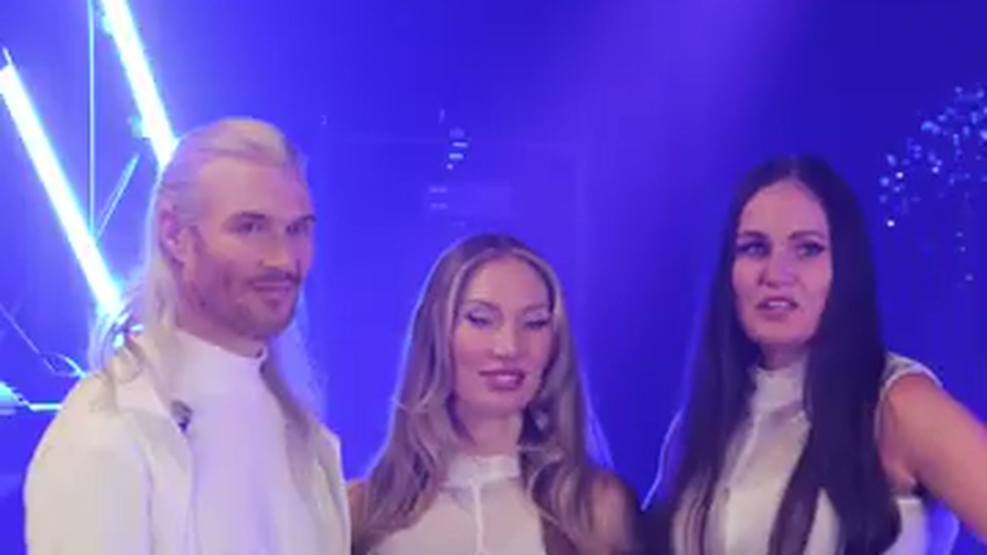 The VYNILYN trio in white stage outfits under blue lighting during an interview